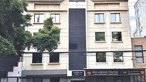 A multi-story building with a central vertical black panel, a gated entrance, and a storefront with signage. - Apartamento loft cali (Cali)