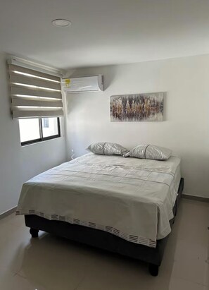 A bedroom with a bed, a window with blinds, an air conditioning unit, and a painting on the wall. - Apartamento loft cali (Cali)
