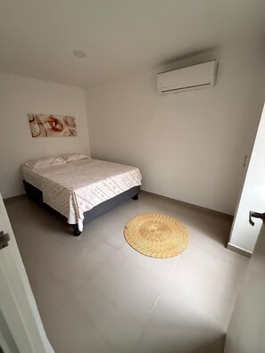 A bedroom with a bed, a woven rug, an air conditioning unit, and a wall-mounted artwork. - Apartamento loft cali (Cali)