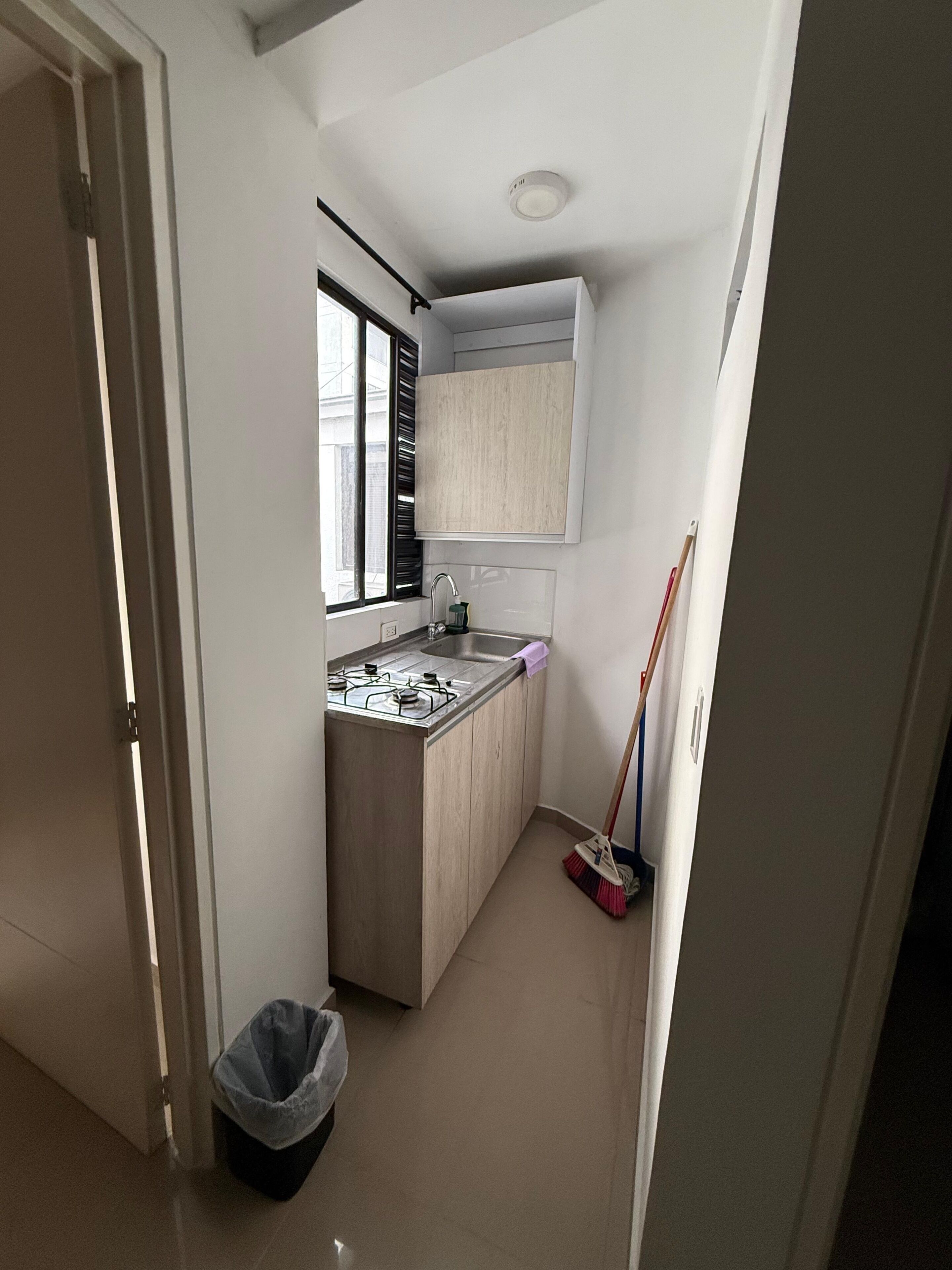 A compact kitchen with a gas stove, a sink, and a window with blinds.