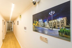 A hallway with a large painting of a historic building, a security camera, and a sign indicating directions.
