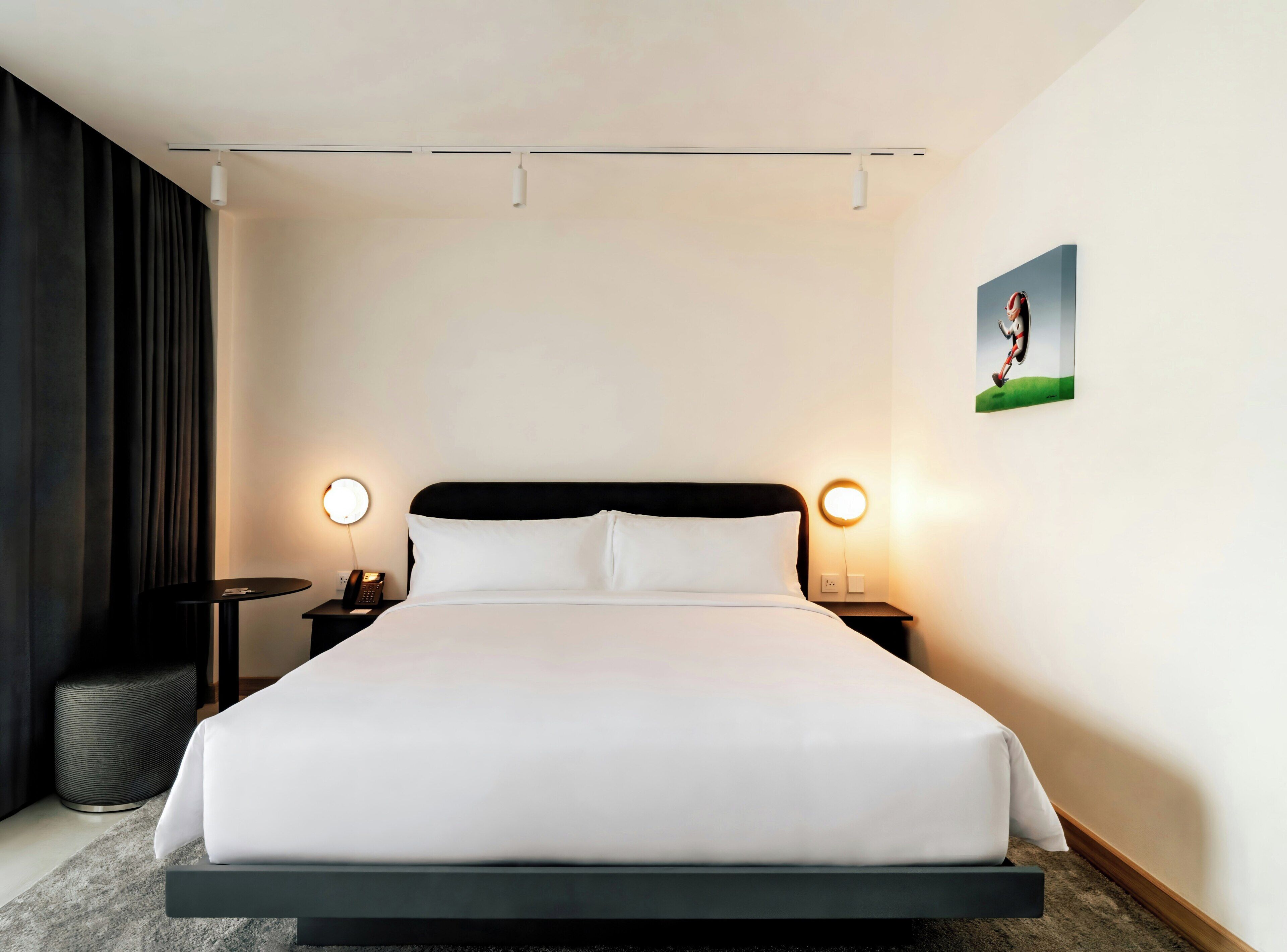 A hotel room with a large bed, two bedside tables with lamps, a wall-mounted picture, and a curtain on one side.