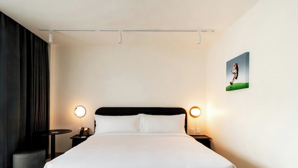 Ein Hotelzimmer mit einem großen Bett, zwei Nachttischen mit Lampen, einem Wandbild und einem Vorhang an einer Seite.