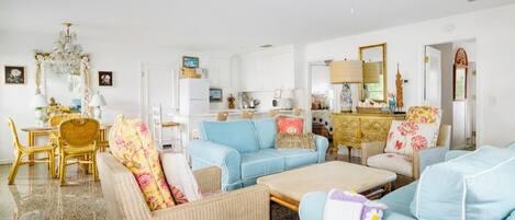 A spacious living room with a dining area, a kitchen, and a large chandelier.