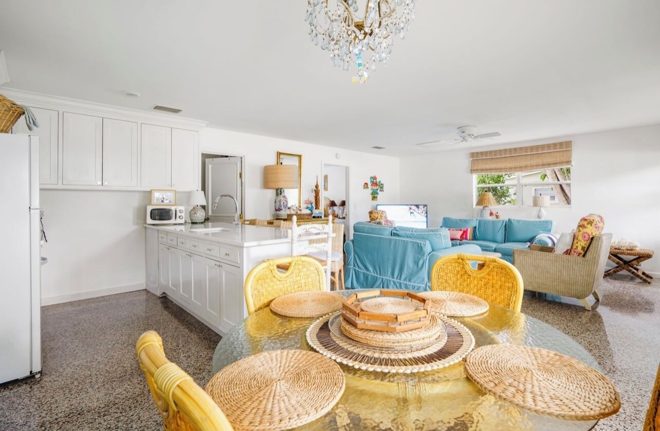 A spacious living area with a dining table, wicker chairs, a blue sofa, and a chandelier.