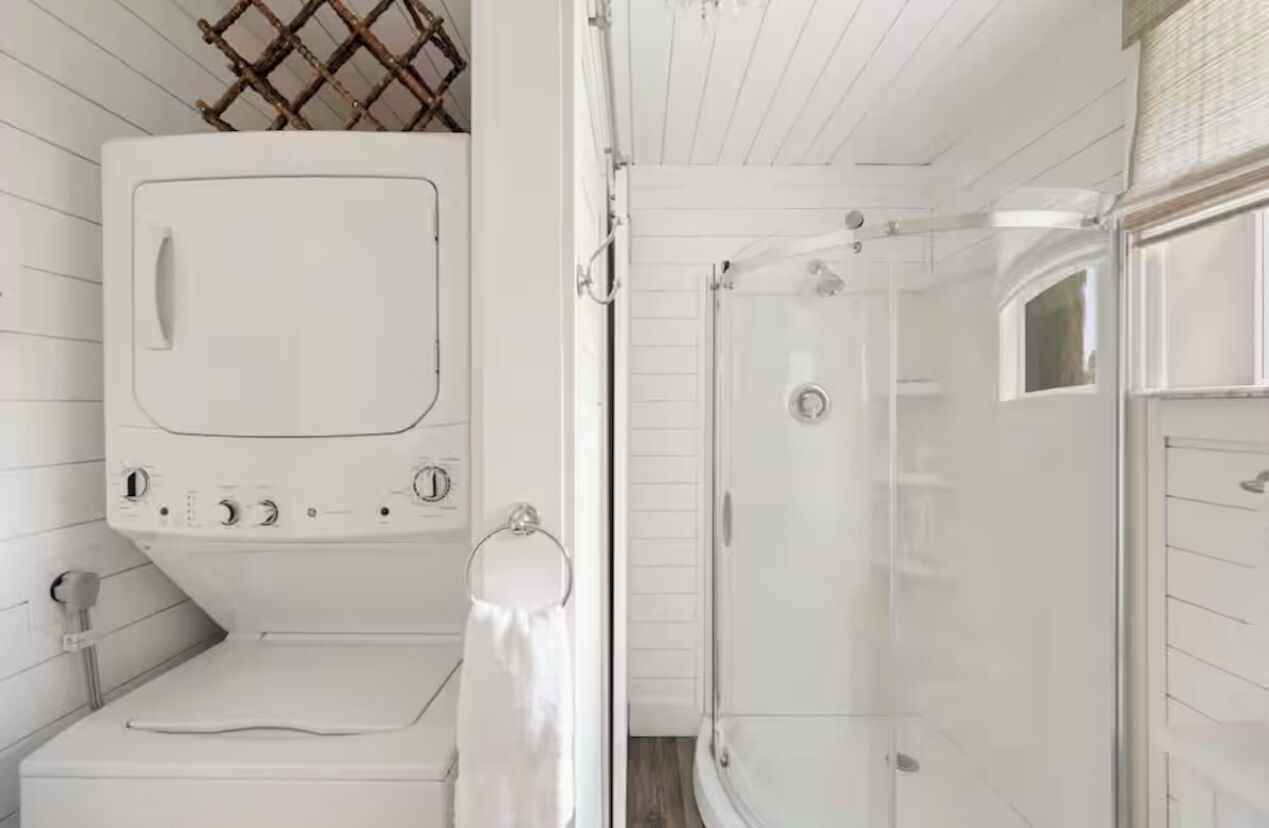 Et lille badeværelse med vaskemaskine, brusebad og toilet.