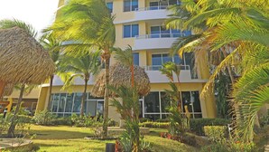 Ein hohes, mehrgeschossiges Hotel mit Balkonen, umgeben von Palmen und einem gepflegten Garten.