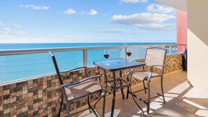 Ein Balkon mit Blick auf das Meer, zwei Stühle, ein Tisch und zwei Weingläser.