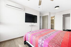 Un dormitorio con cama, televisión de pantalla plana, aire acondicionado y piso de madera.