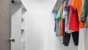 Ein begehbarer Kleiderschrank mit hängender Kleidung, einem Wäschekorb und einer Tür mit einem runden Knauf.