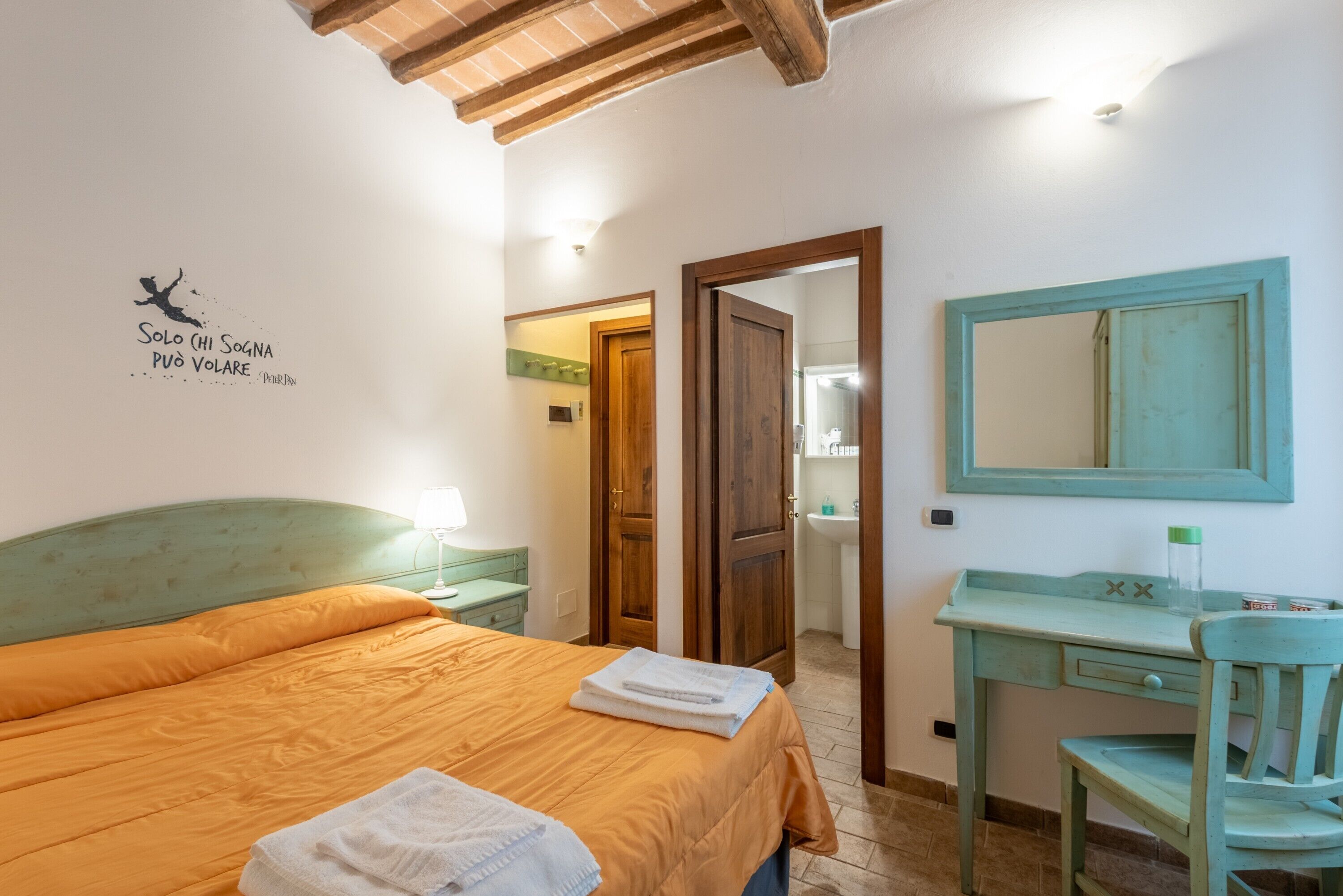 A bedroom with a bed, a desk, a chair, a mirror, and a door leading to a bathroom.
