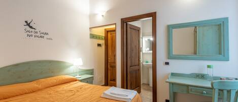 A bedroom with a bed, a desk, a chair, a mirror, and a door leading to a bathroom.