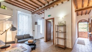A cozy room with a sofa, a small table, a lamp, a wooden shelf, and a door leading to another room.