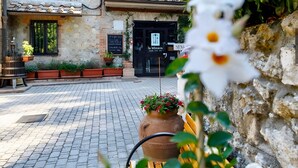 A rustic building with a stone facade, a black door with signage, and a paved courtyard.