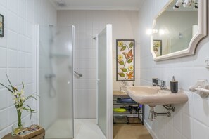 A bathroom with a shower, sink, mirror, and a decorative flower painting on the wall. - Holiday Home 'Mudarra Conil' with Private Terrace, Wi-Fi and Air Conditioning (Conil de la Frontera)