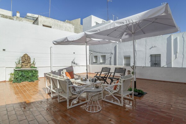 A rooftop patio with white wicker furniture, a white umbrella, and a statue. - Holiday Home 'Mudarra Conil' with Private Terrace, Wi-Fi and Air Conditioning (Conil de la Frontera)
