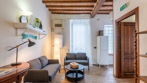 A living room with a sofa, a coffee table, a lamp, a shelf with a clock and a plant, and a door with a sign. - Podere La Miniera Relax-Food, room with garden view (Siena)
