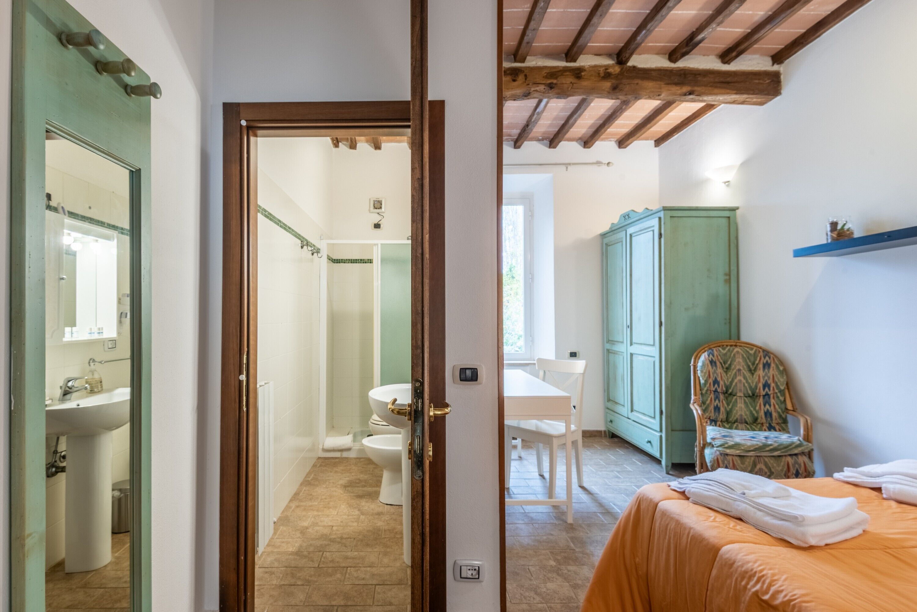Una stanza con un letto, una sedia, un armadio e una porta che dà su un bagno.