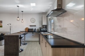 Une cuisine moderne dotée d’un îlot central, d’appareils électroménagers en acier inoxydable et de luminaires suspendus.
