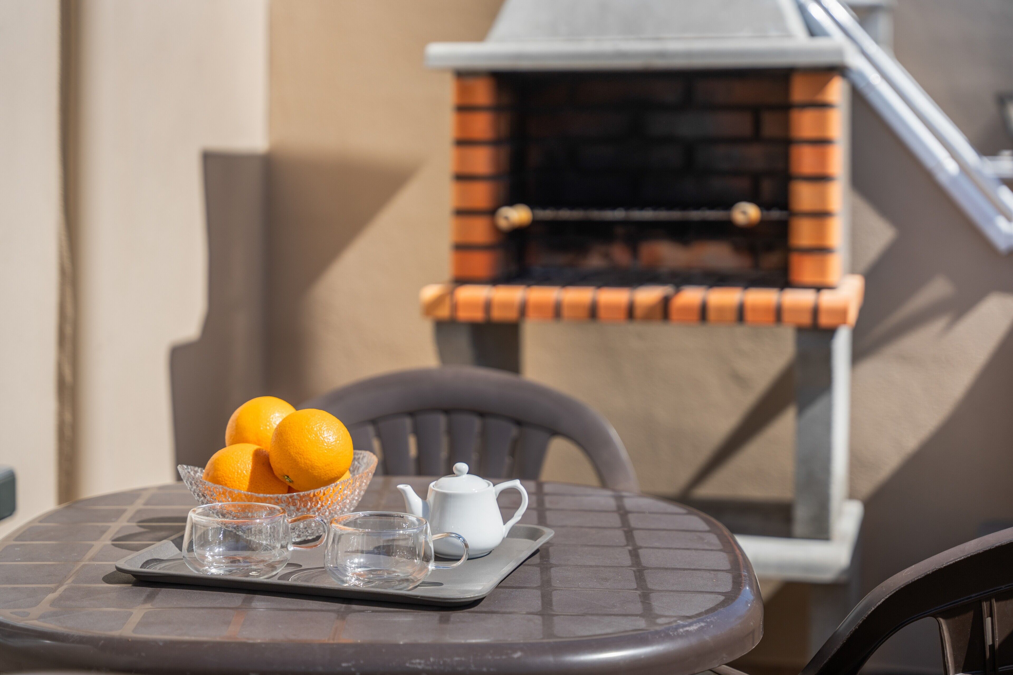 A table with a glass bowl of oranges, a white teapot, and two glasses on a tray.