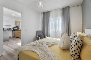 Moderni hotellihuone, jossa on sänky, työpöytä, tuoli, pieni keittiö ja näkymä ulos.