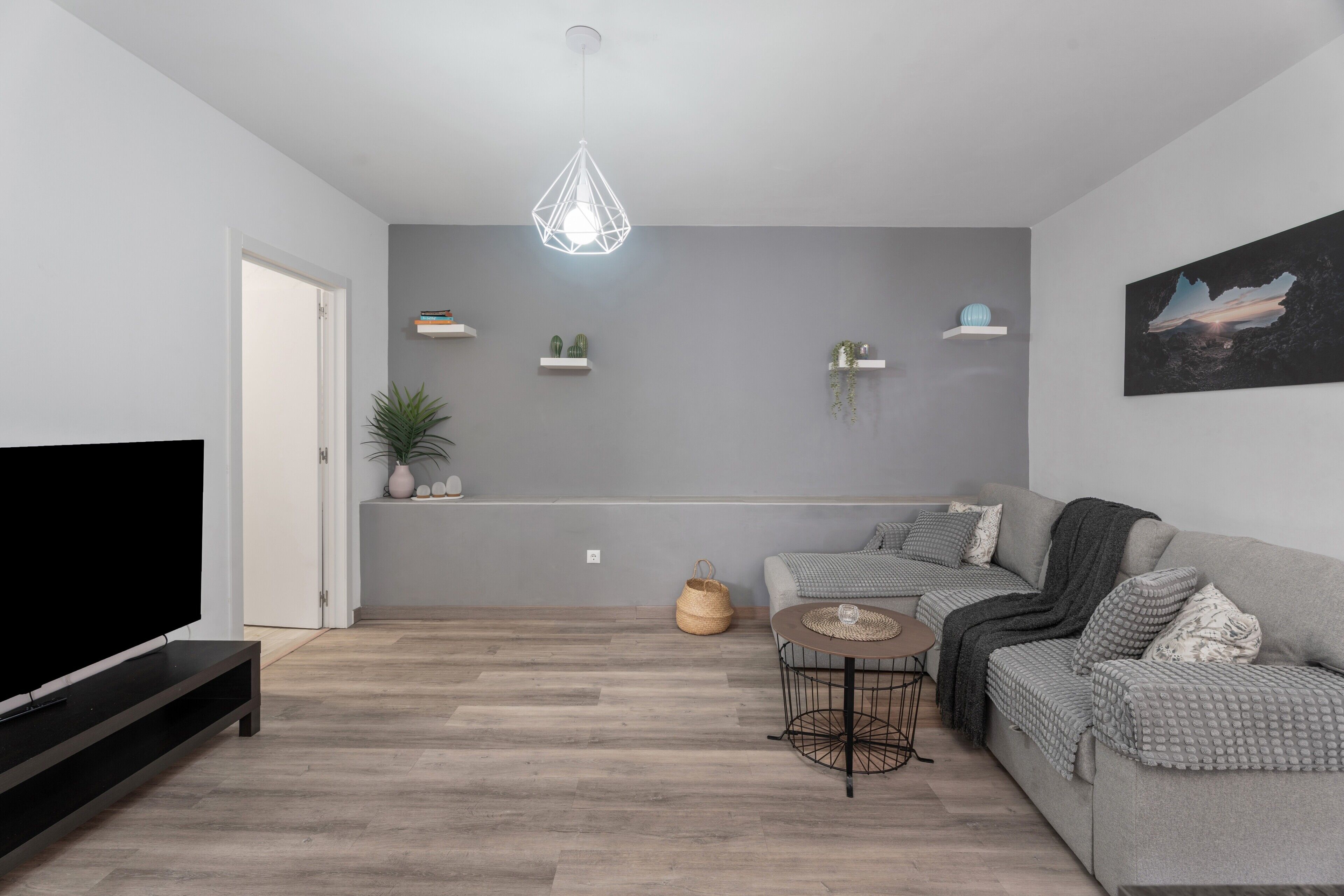 Una sala de estar moderna con un televisor de pantalla plana, un sofá gris, una mesa de centro y una lámpara colgante.
