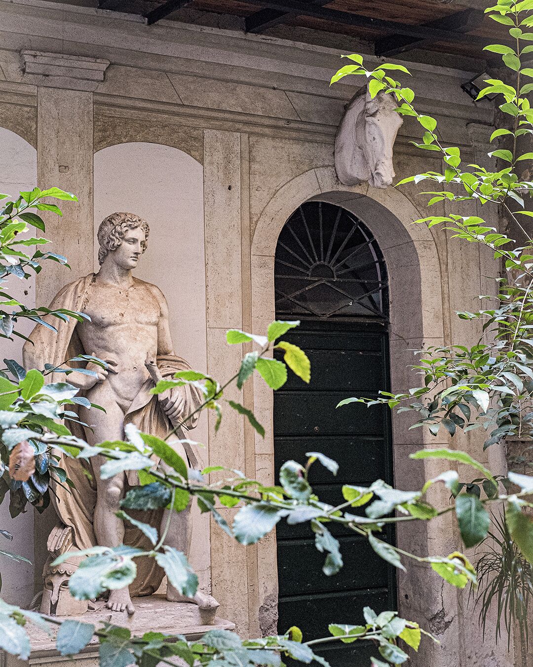 Una statua classica di fronte a un edificio in pietra con un portale ad arco.