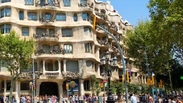 Un immeuble à plusieurs étages, doté de balcons, devant lequel se trouve une foule de personnes.