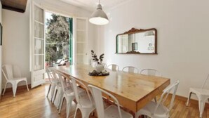 Un coin repas avec une table en bois, des chaises blanches, une suspension et un miroir au mur.