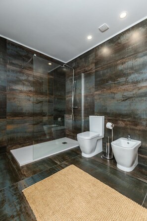 A modern bathroom with a glass-enclosed shower, a toilet, a bidet, and a sink.