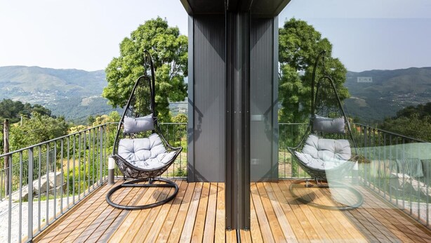 En balkon med to hængestole, et træterrasse og udsigt over landskabet.