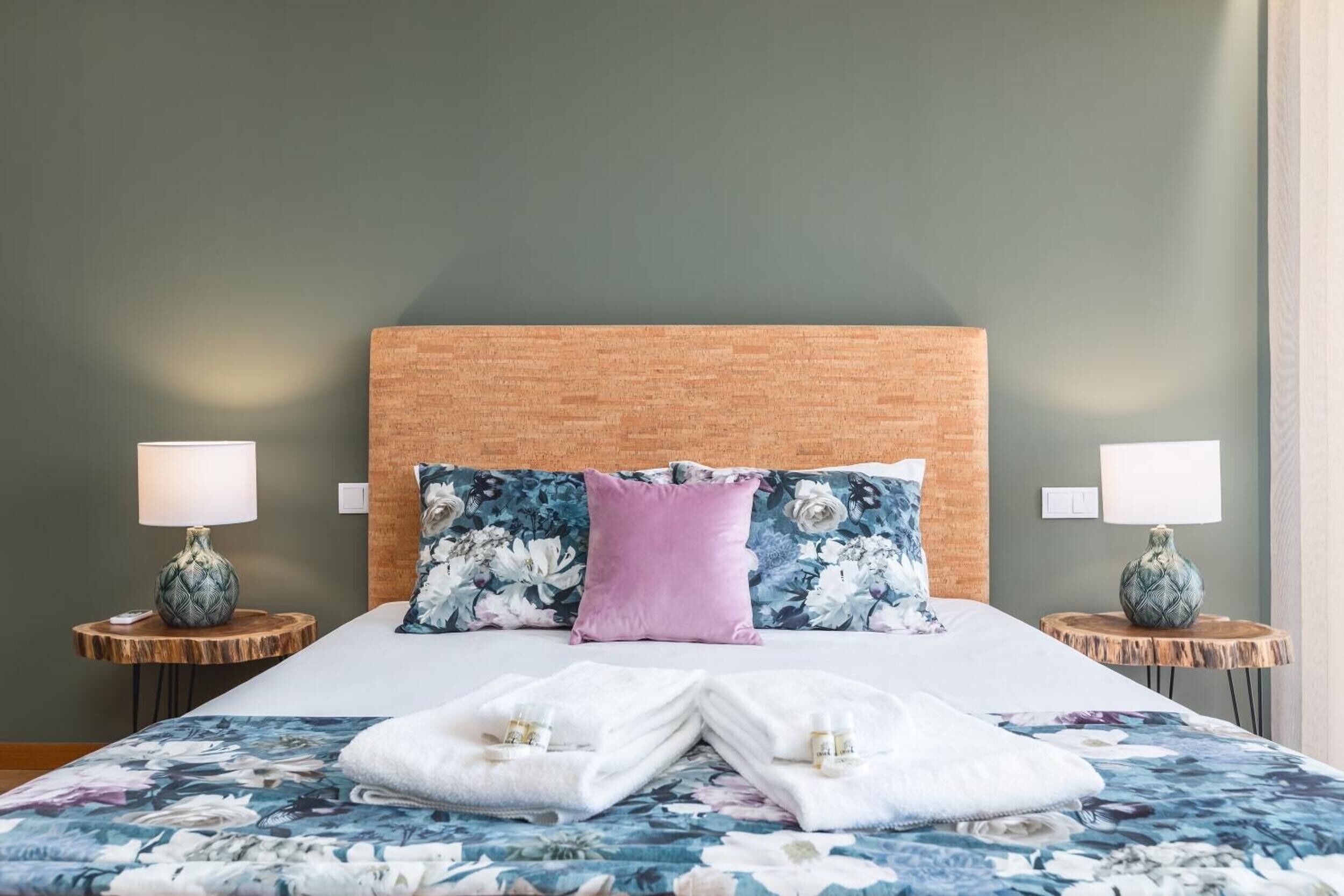 A hotel room with a large bed, floral bedding, two bedside tables with lamps, and a wooden headboard.