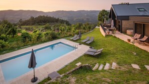 A swimming pool with lounge chairs, a patio with a table and chairs, and a view of the hills.