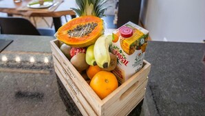 A wooden crate filled with fruits and a carton of juice on a kitchen counter.