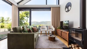 A modern living room with a sofa, chairs, a TV, a fireplace, and a large window overlooking a scenic view. - Chalet 'Casas De Bouro 3 Do Alecrim' with Private Sauna and Jacuzzi (Terras de Bouro)