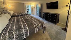 Un dormitorio con una cama grande, un aparador, un televisor montado en la pared y vistas al exterior a través de una puerta.