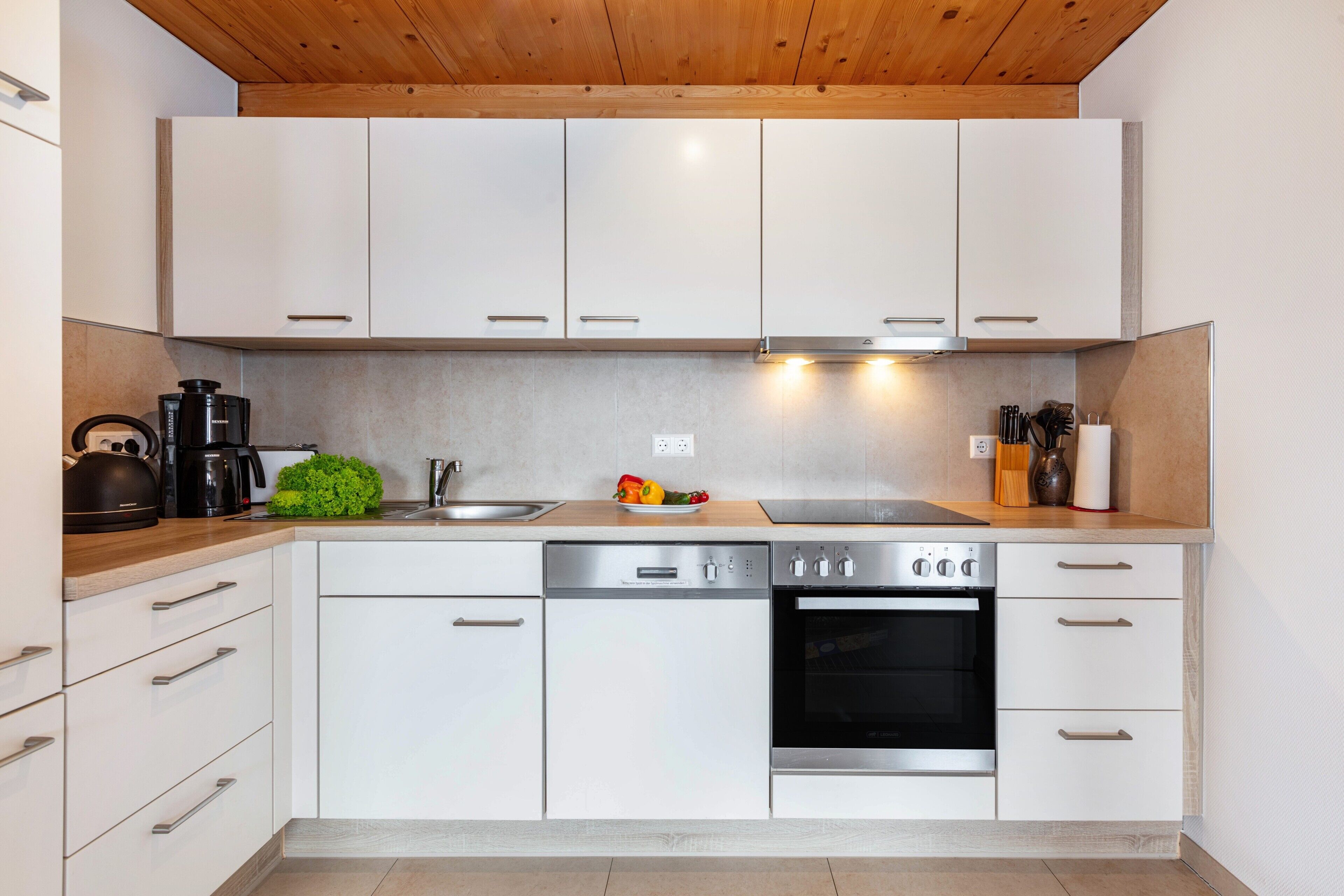 A modern kitchen with white cabinets, stainless steel appliances, a wooden countertop, and a built-in oven.
