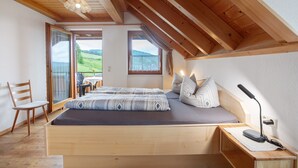 Une chambre avec un plafond en bois, un lit avec un matelas gris, une table de chevet avec une lampe et une chaise.