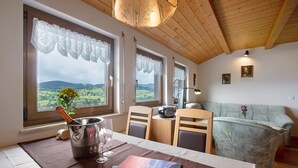 Une pièce avec une table dressée pour deux personnes, une bouteille de champagne et une vue sur la campagne, visible à travers de grandes fenêtres.