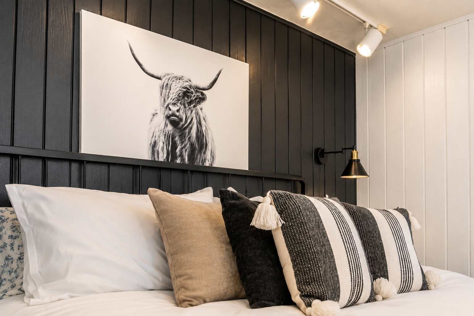 A bed with white and patterned pillows, a black and white striped pillow, and a black lamp on a wall with a black and white striped pillow hanging below.
