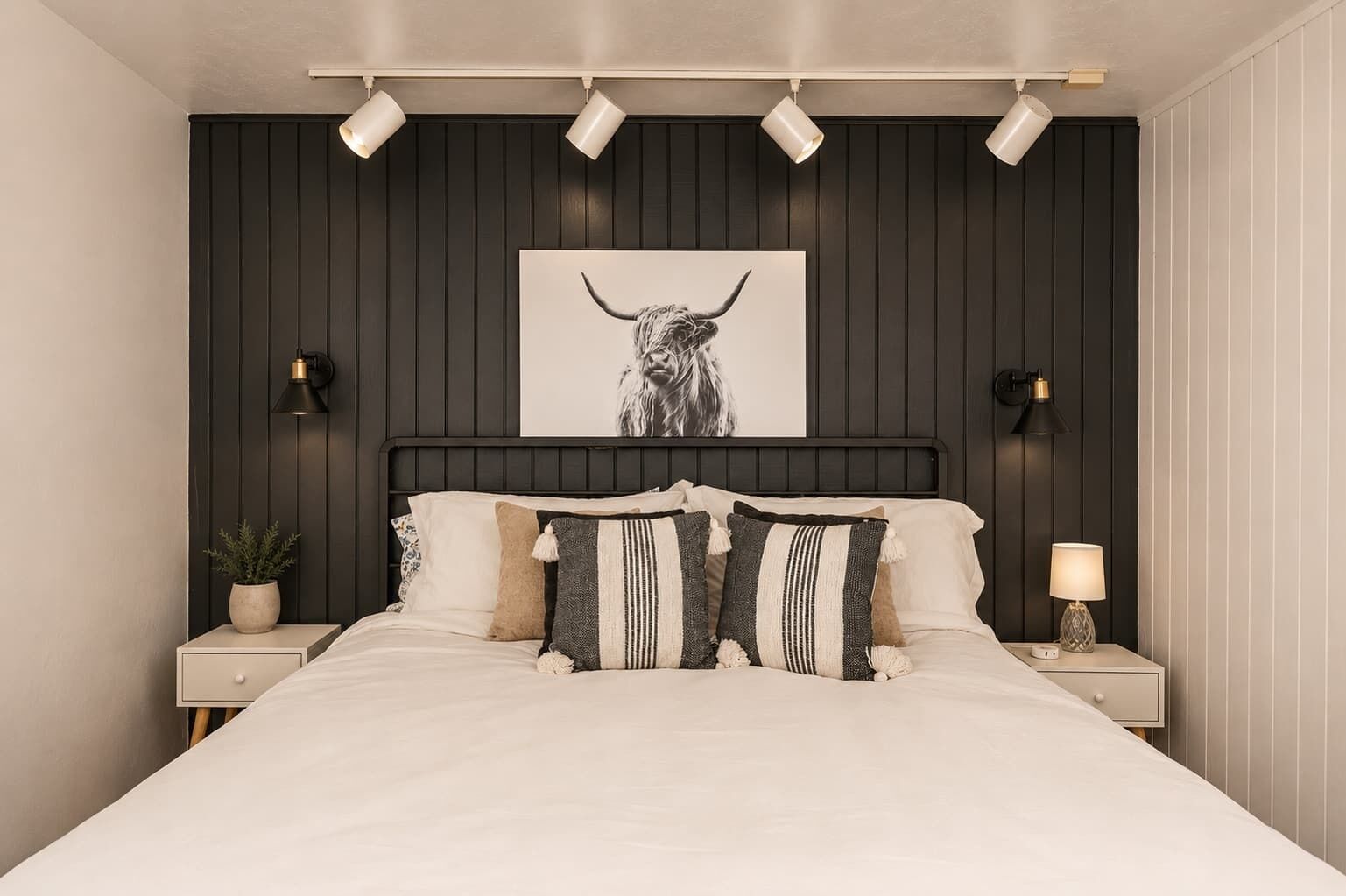 A bedroom with a bed, a wall-mounted artwork of a bull, bedside lamps, and a potted plant.
