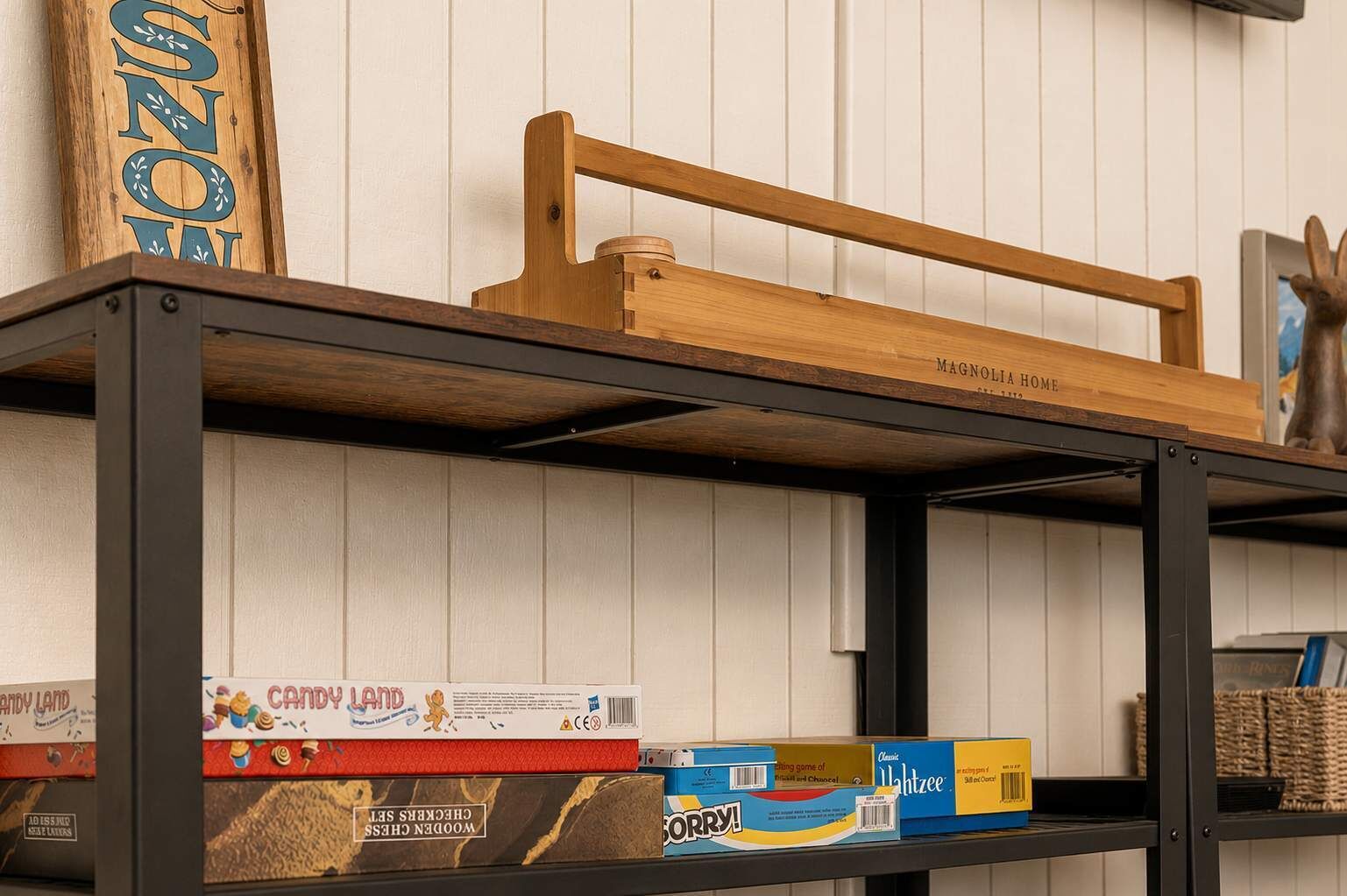 A wooden shelf with a sign that reads 'MAGNOLIA HOME' and various board games and boxes on the lower shelf.