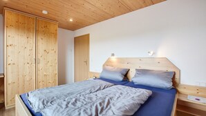 Een slaapkamer met een houten plafond, een bed met blauw beddengoed, een nachtkastje en een kledingkast.