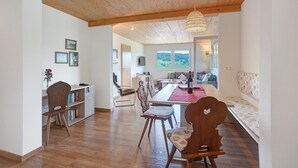 Een kamer met een houten plafond, een eettafel met stoelen, een boekenkast en een raam met uitzicht.