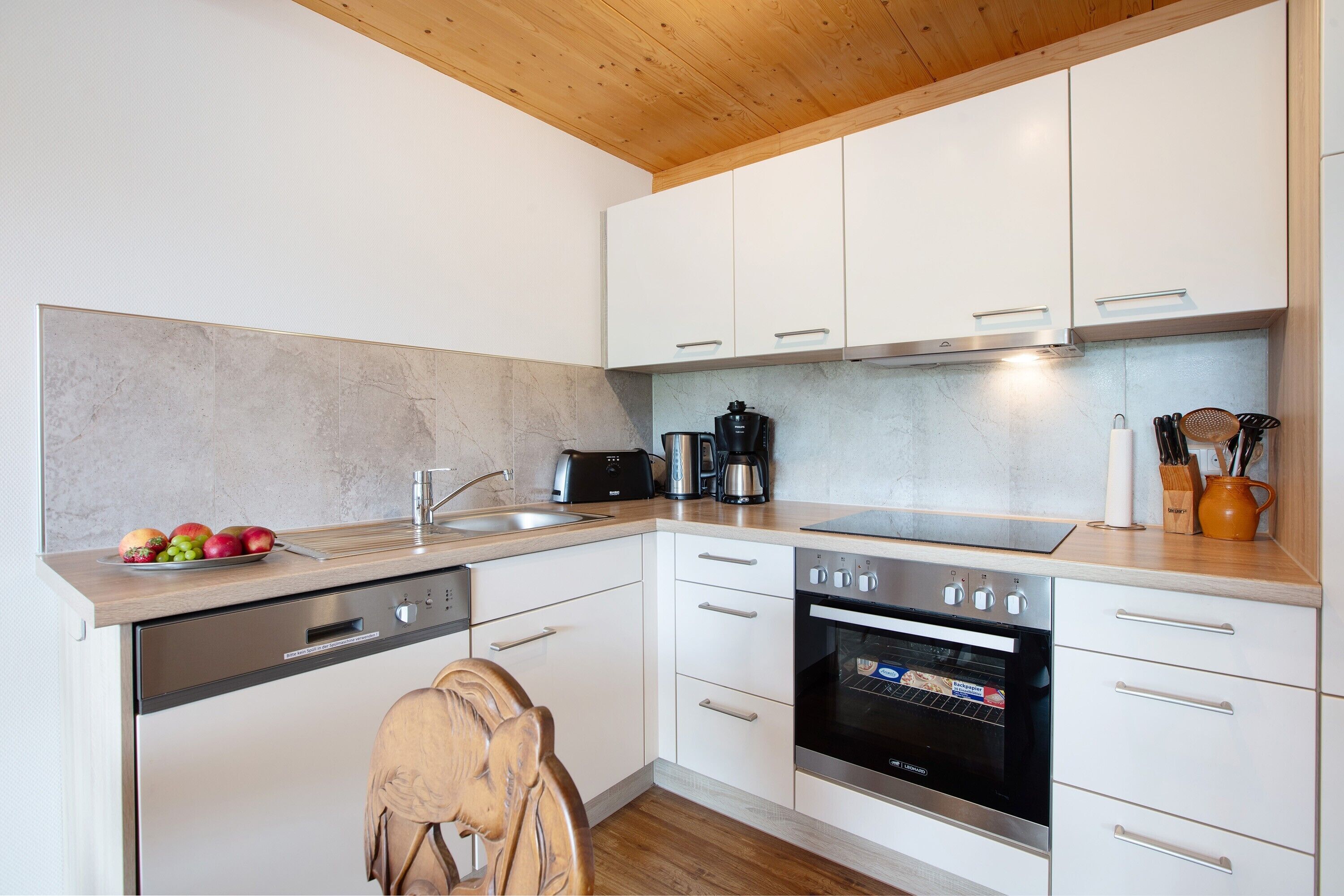 A modern kitchen with white cabinets, a dishwasher, an oven, and a coffee maker.