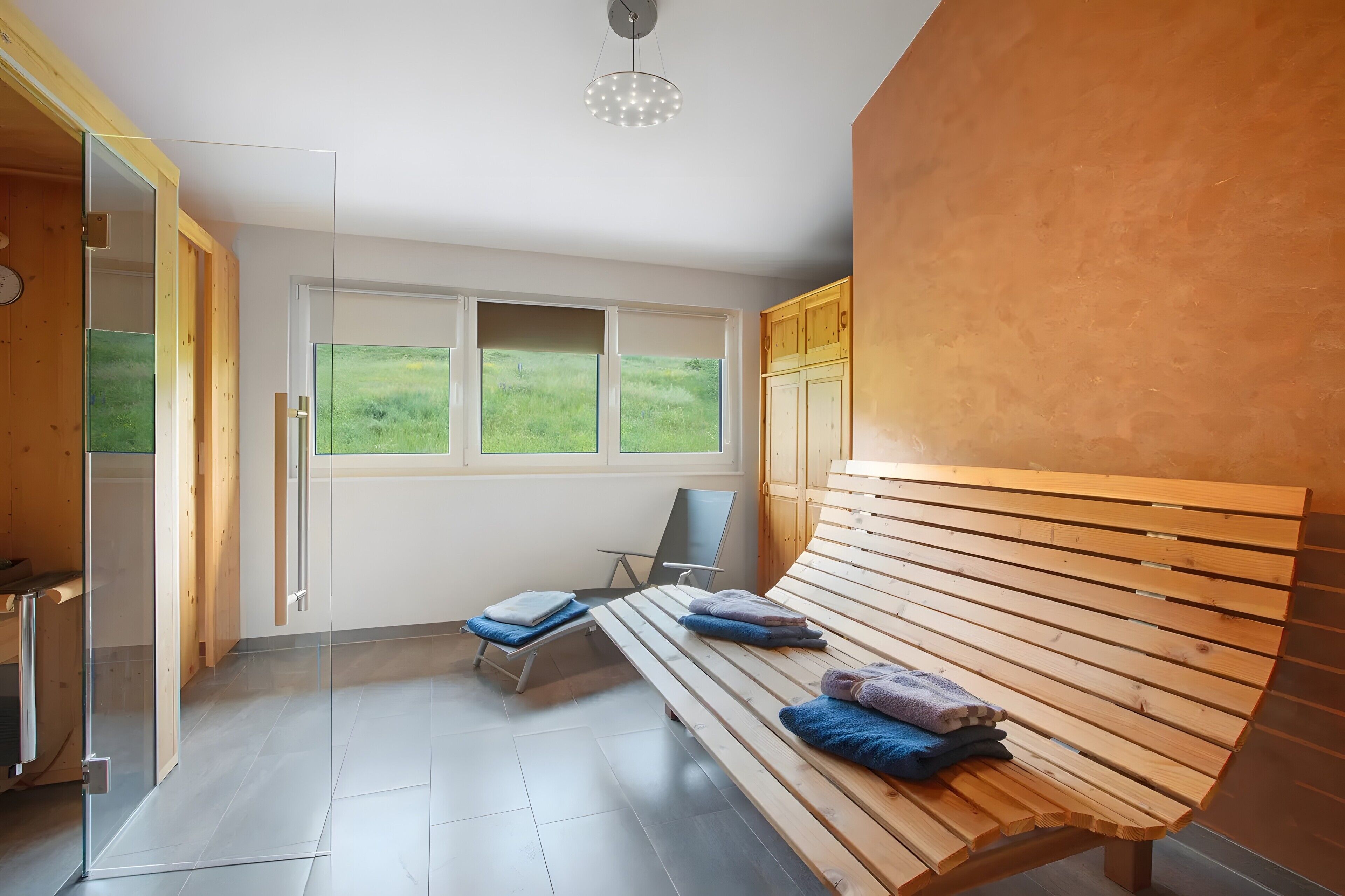 A modern room with a bench, a chair, and a view of a green field through the window.
