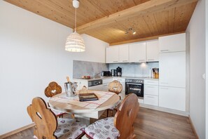 Una cocina moderna con armarios blancos, techo de madera y una mesa de comedor con sillas de estampado de corazones.