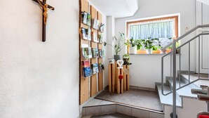 A staircase with a metal handrail, a wooden cross on the wall, and a window with a curtain. - Haus Hochtalblick Apartment "Rechberg" with Panoramic View, Wi-Fi, DreiWelten-Card Included (Bernau im Schwarzwald)