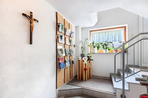 A staircase with a metal handrail, a wooden cross on the wall, and a window with a curtain. - Haus Hochtalblick Apartment "Rechberg" with Panoramic View, Wi-Fi, DreiWelten-Card Included (Bernau im Schwarzwald)