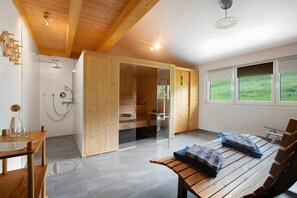 A modern room with a wooden ceiling, a sauna, a glass shower enclosure, a wooden bench, and large windows.